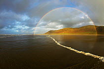 Incoming tide and double rainbow caused by precipitation and wave spray, with house on the Rhosilli down coastline. West-facing beach in Rhosilli Bay, Gower Peninsular, Area of Outstanding Natural Bea...