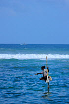 Traditional fishermen of Weligama, seated on long poles, fishing with rods, Sri Lanka, June 2010