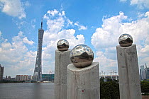 Sculptural concrete pillars holding polished steel spheres with 610m Guangzhou TV and Sightseeing Tower visible across Zhujiang River. Guangdong, China. For Editorial use only.
