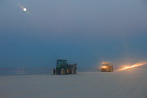 Oil spill response vehicles grooming a white sand beach before sunrise. Many clean up efforts from the BP Deepwater Horizon oil leak were cosmetic in nature and aimed to cover up the damage. These veh...