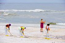 Beach cleaners, and a woman taking a cell phone photo of the oil contamination, resulting from the BP Deepwater Horizon oil leak in the Gulf of Mexico, Orange Beach, Baldwin County, Alabama, USA, June...