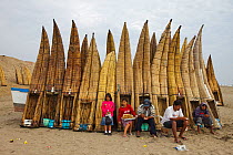 Fishermen of Totora sitting with their upturned reed canoes on Pimentel beach, Chiclayo, Peru, November 2009
