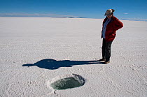 Tourist standing by hole in Salar de Uyuni, the worlds largest salt pan, Altiplano, Bolivia. February 2009.