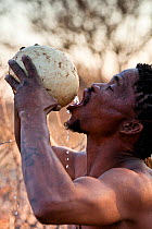 Qhaikgao, a Kalahari bushman, drinking water from an ostrich's egg in the dry season. Kalahari Desert, Botswana, August 2008
