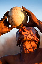 'Xamse', a young Kalahari bushman, drinking water from an ostrich's egg in the dry season, egg was buried underground during the rainy season. Kalahari Desert, Botswana, August 2008