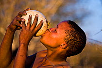 'Xamse', a young Kalahari bushman, drinking water from an ostrich's egg in the dry season, egg was buried underground during the rainy season, Kalahari Desert, Botswana, August 2008