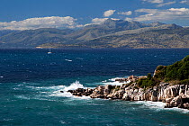Passenger ferry negotiating choppy sea along north east coast of Corfu, Greece, with Albanian mountains in the background, June 2010.