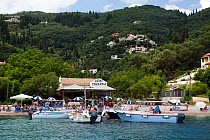 Agni Taverna, one of several restaurants located on the beach in San Stefanos Bay, with customers' boats moored off the jetty, Corfu, Greece, June 2010.