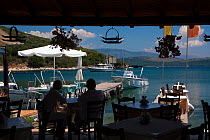 Couple sitting in a beachside restaurant in San Stefanos Bay, with the mountains of Albania visible in the distance. Corfu, Greece, June 2010.