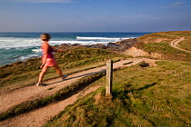 Woman walking in the early morning along the South West Coast Path from Booby's Bay towards Trevose Head, Cornwall Area of Outstanding Natural Beauty (AONB), England, August 2010. Model released.