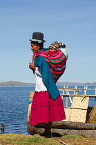 Aymara mother acarrying her babyon her back, standing near the  edge of  Lake Titicaca, Bolivia, South America 2008