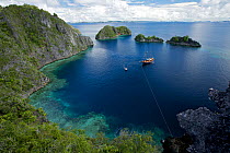 The ship Shakti, chartered for a GEO Expedition, is tied off in small bay surrounded by limestone cliffs and islets. Misool Island vicinity. Near smaller island of Fiabacet. West Papua, Indonesia, Apr...