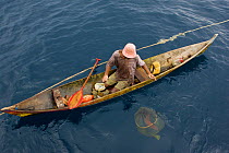 At sea off the Fak Fak Peninsula, a lone fisherman in a canoe has caught a variety of fish including jacks, snappers, and groupers. Visible below the water, is a net holding a grouper he is keeping a...