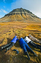 Four people lying on ground photographing Arctic / Scheuchzer's cotton grass (Eriophorum scheuchzeri) Edgeoya (Edge Island) Svalbard, Norway 2010