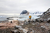 Visitors and Gentoo Penguin (Pygoscelis papua) against dramatic landscape at Port Charcot, Booth Island, Antarctica, February 2009.