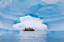 Zodiac filled with tourists seen through ice arch in an iceberg, Pleneau Island, Antarctica, February 2009.