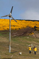 Yellow jacketed tourists by wind turbine on West Point Island, Falkland Islands, 2009.