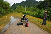 Man with motorbike looking at road impasssable after flooding, Phong Nha Ke Bang National Park, Vietnam.
