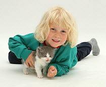 Portrait of young blonde haired girl, lying down with grey-and-white kitten. Model released