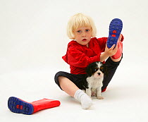 Young blonde haired girl, sitting with King Charles Spaniel puppy and taking off welly boots. Model released