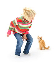 Yonng girl with blonde hair leaping about and scaring a ginger kitten. Model released