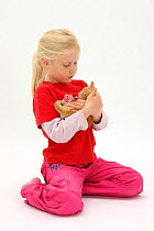Portrait of young girl with blonde hair, aged 7, holding a ginger kitten, aged 7 weeks. Model released