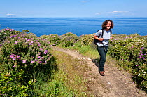 Woman walking through garigue coastland, with flowering rockroses (Cistus) and other plants, Giglio island, National Park of the Tuscany archipelago, Italy, May 2010. Model released