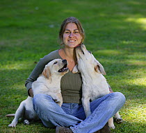 Woman sitting on grass with two yellow Labrador Retriever puppies