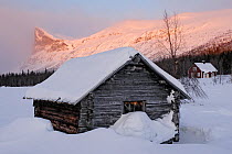 Traditional wooden farm hut beside Lake Laitaure, with Skierfe mountain in the background, Aktse, Laponia, Sweden, sunrise, winter