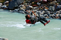 Alpinist mountaineer crossing the Fitz Roy river with a tyrolean crossing (also called zip-line, flying fox, zip wire, aerial runway, death slide), Los Glaciares National Park, Patagonia, Argentina, J...