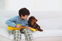 Portrait of young boy sitting and playing toy guitar, with Longhaired Dachshund on his lap