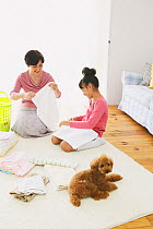 Portrait of mother and daughter sitting folding towels, with Toy Poodle puppy
