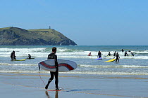 Surfers heading out into the waves at Polzeath beach. Cornwall, UK, April 2010.