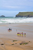Surf school practising balancing on surf boards on the beach before entering the sea. Polzeath, Cornwall, UK, April 2010.