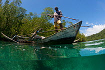 Split-level of a shallow coral reef and mangroves with local West Papuan man in a dugout canoe. North Raja Ampat, West Papua, Indonesia, February 2010