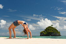 Young woman in "bridge" yoga pose on a sandy beach. Daram Island, Raja Ampat, West Papua, Indonesia, January 2010, model released.