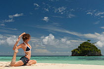 Young woman in a yoga pose on a sandy beach. Daram Island, Raja Ampat, West Papua, Indonesia, January 2010.