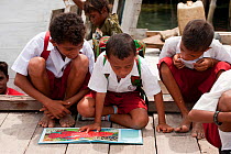 Boys from the Yellu Village school reading a book about the underwater world. Misool, Raja Ampat, West Papua, Indonesia, January 2010.