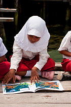 A girl from the Yellu Village school reading a book about the underwater world. Misool, Raja Ampat, West Papua, Indonesia, January 2010.