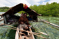West Papuan fisherman paddling in a traditional outrigger house boat. Raja Ampat, West Papua, Indonesia, February 2010.