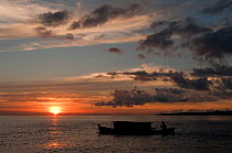 West Papuan fisherman in his outrigger house boat at sunset. Raja Ampat, West Papua, Indonesia, February 2010.