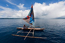 West Papuan fisherman in his outrigger dugout canoe with sails. Raja Ampat, West Papua, Indonesia, February 2010.