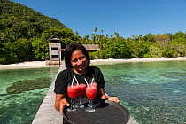 Woman bringing welcome drinks to the jetty of Sorido Bay Resort. Raja Ampat, West Papua, Indonesia, February 2010.
