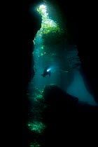 Light streaming into a shallow cave in a dive site called The Passage, with a diver swimming through. North Raja Ampat, West Papua, Indonesia, February 2010.