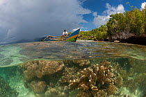 Split-level shot of a shallow coral reef with local West Papuan man in his dugout canoe. North Raja Ampat, West Papua, Indonesia, February 2010.