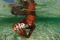 Papuan boy swimming in the shallows holding his pet baby hawksbill turtle (Eretmochelys imbricata). Tunnung Island, New Hanover, Papua New Guinea, June 2010.