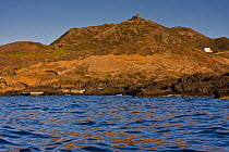 Linosa, island of Sicily. View from the sea of the northern coast, with igneous rocks and ancient observation tower on the highest mountain. Italy, July.