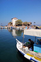 Fisherman preparing bait on his boat in Skala Sikaminia harbour with chapel in the background. Lesbos / Lesvos, Greece, August 2010