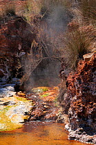 Boiling water from hot springs flowing into thermal river, with colourful growths of blue-green algae and mineral deposits at margins. Polychnitos, Lesbos / Lesvos, Greece, August 2010.