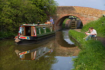 Men fishing beside longboat on the Grand Union Canal at Marsworth, Hertfordshire, UK, May